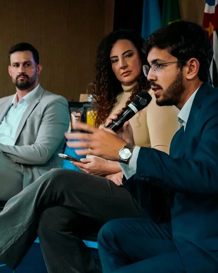 Guilherme Bastos, de terno azul, falando ao microfone num painel